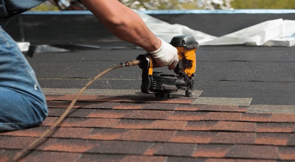 Un ouvrier portant des gants qui utilise un pistolet pour installer des shingles sur un toit