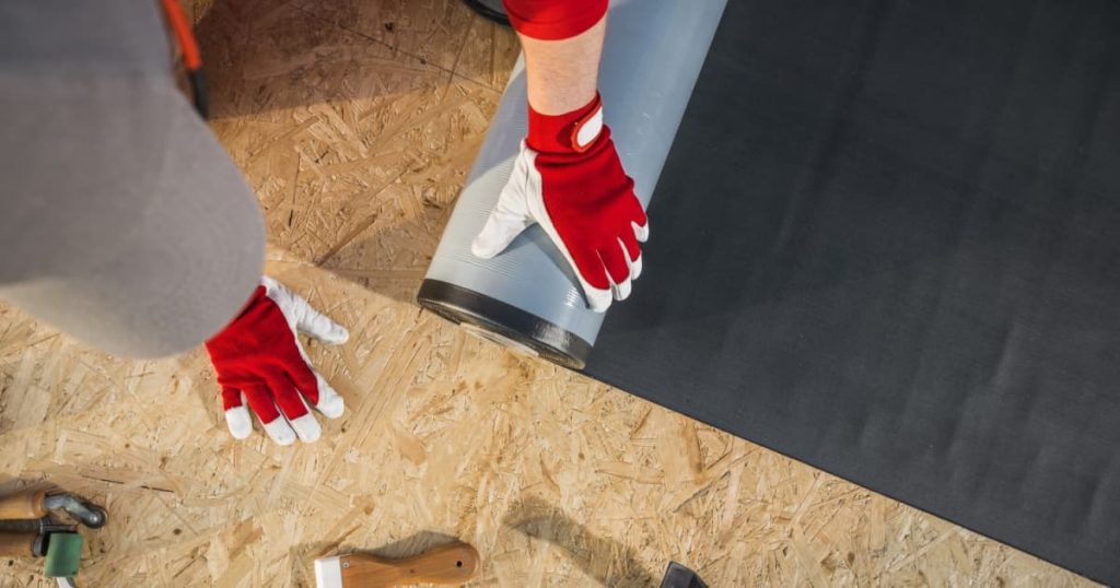 homme qui pose avec des gants une membrane EPDM sur toit plat