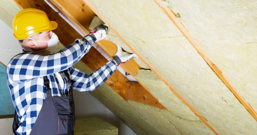 Ouvrier installant de la laine de verre sous une toiture inclinée pour l’isolation thermique.