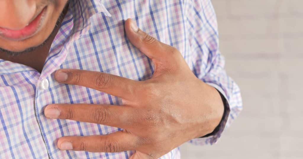 Homme avec une chemise à carreau de face dont la main gauche est posée sur le côté gauche de sa poitrine.