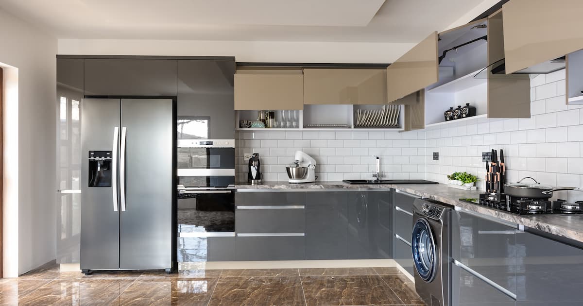 Cuisine grise en forme L avec frigo et machine à laver et carrelage effet marbre au sol