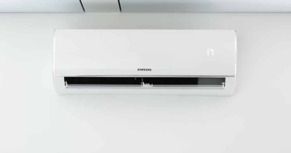 Un climatiseur mural Samsung, un appareil de haute qualité, installé contre un mur blanc, juste en dessous d’un plafond blanc.