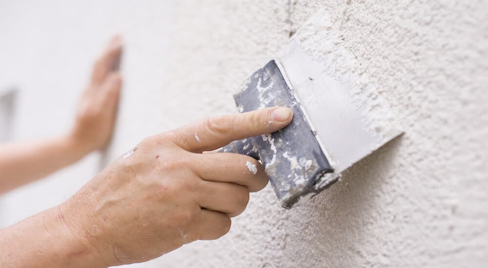 Application du crépi sur une façade à l'aide d'une spatule. 