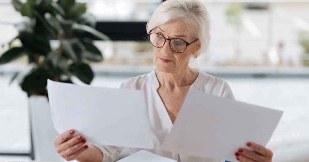Une retraitée compare deux documents papier pour choisir la meilleure offre d'assurance hospitalisation. 