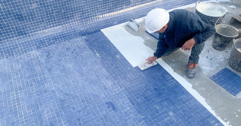 Un spécialiste en train de carreler une piscine extérieur