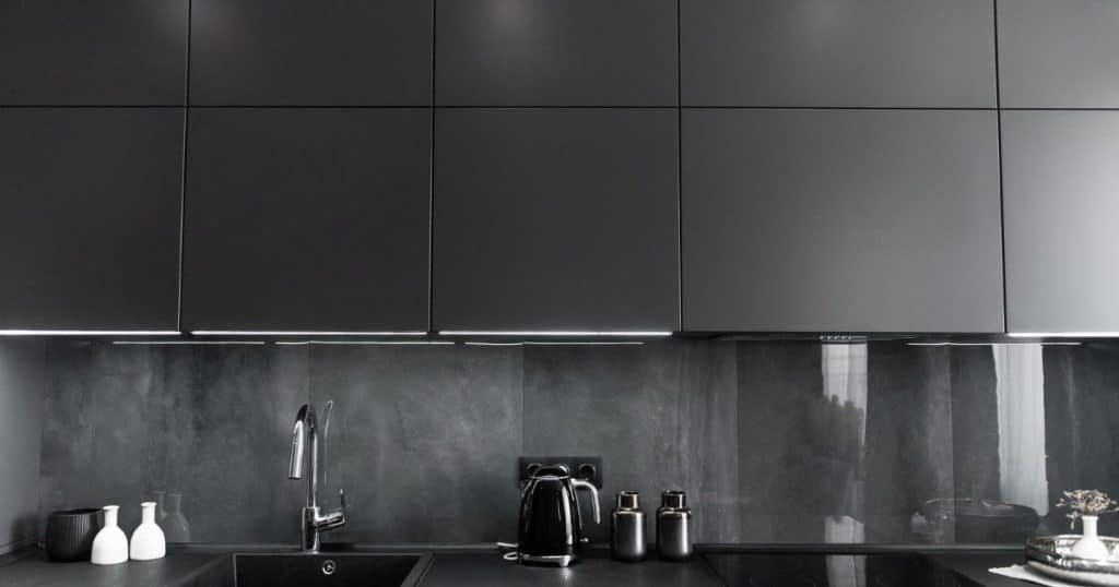 Cuisine anthracite moderne avec armoires mates, crédence en pierre foncée, évier noir et accessoires en acier inoxydable et céramique.