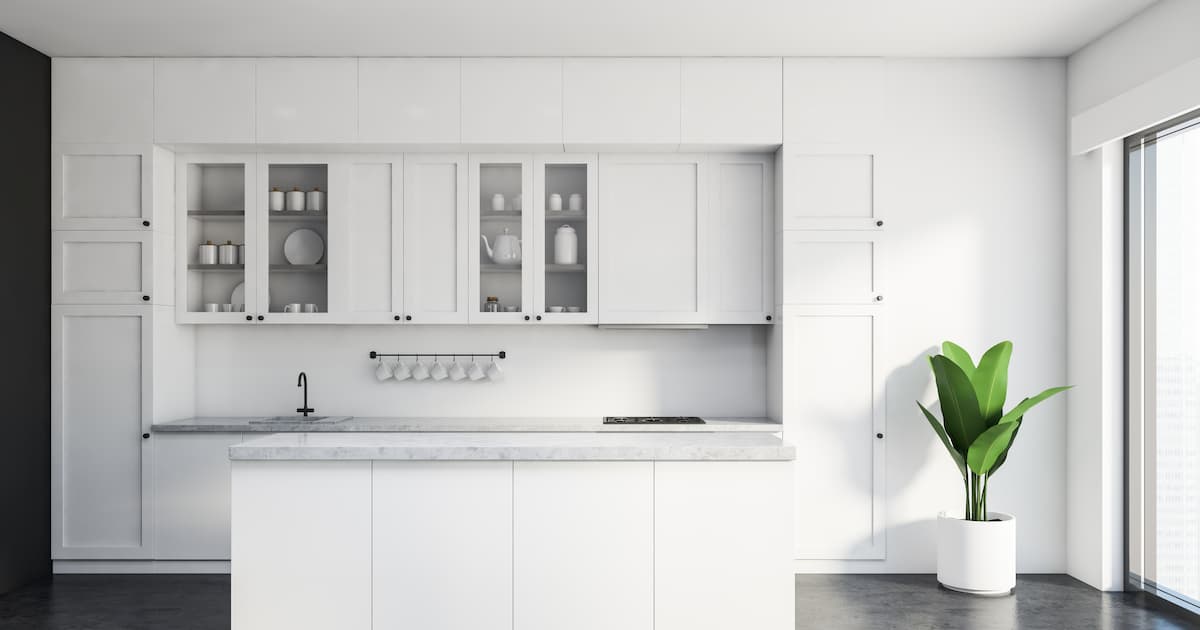 Intérieur de la cuisine classique avec murs blancs et gris, sol en béton, plans de travail et placards blancs et île blanche confortable.