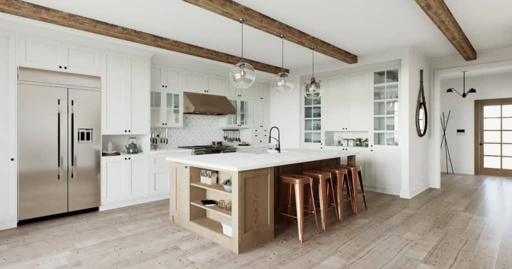 Une cuisine blanche avec un frigo américain, un parquet, un ilot central en bois et blanc, un évier et des chaises hautes en dessous de trois luminaires.