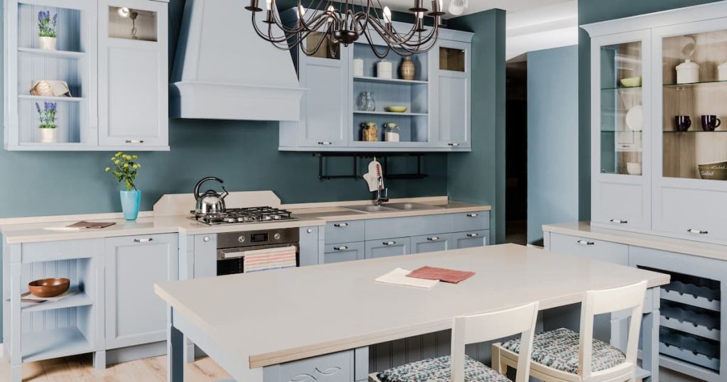 Intérieur d'une cuisine moderne et lumineuse avec des meubles bleus, une table et des chaises en bois blanc.