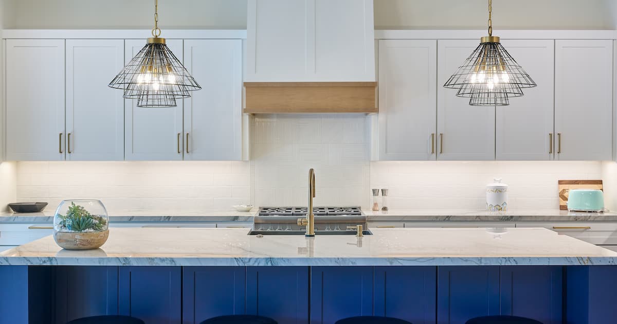 Une cuisine bleue et blanche avec îlot central et 2 lampes accrochées au plafond