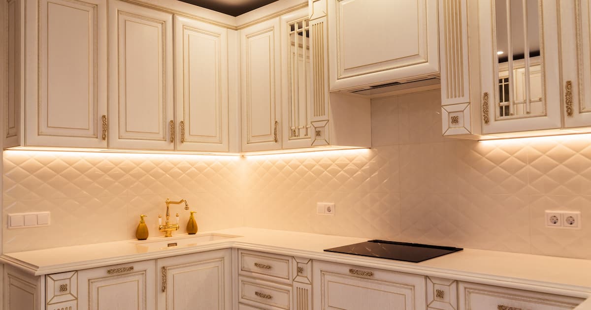 Cuisine blanche élégante avec armoires aux accents dorés et éclairage moderne. Il est équipé d'un rétroprojecteur carrelé, d'appareils intégrés et d'un éclairage LED sous-armoire.