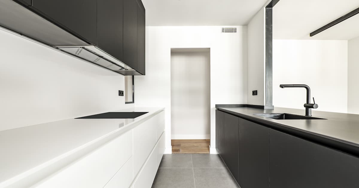 Cuisine meublée avec un mélange de mobilier noir et blanc sans poignées visibles et avec des appareils et des robinets noirs de la même couleur