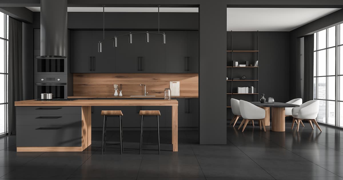 Cuisine intérieure noire avec plan de travail en bois, chaises de bar et coin repas