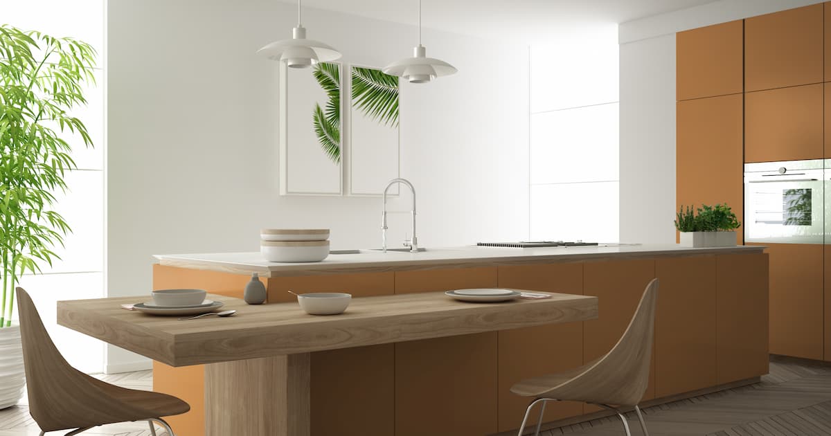 Cuisine moderne et épurée de couleur orange, îlot central et table à manger en bois avec chaises, bambous et plantes en pot