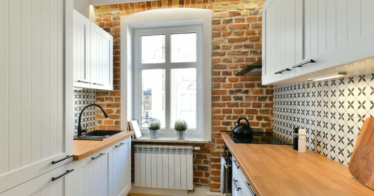 Cuisine rénovée de style rustique avec des armoires blanches à l'intérieur d'une ancienne maison de tenement avec un mur de briques rouges historique exposé éclairé par la lumière LED