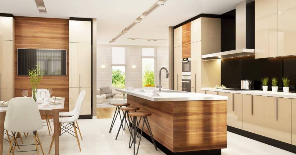 Une cuisine aux tons beiges avec un ilot central avec 3 chaises et une salle à manger, une télé et des plantes