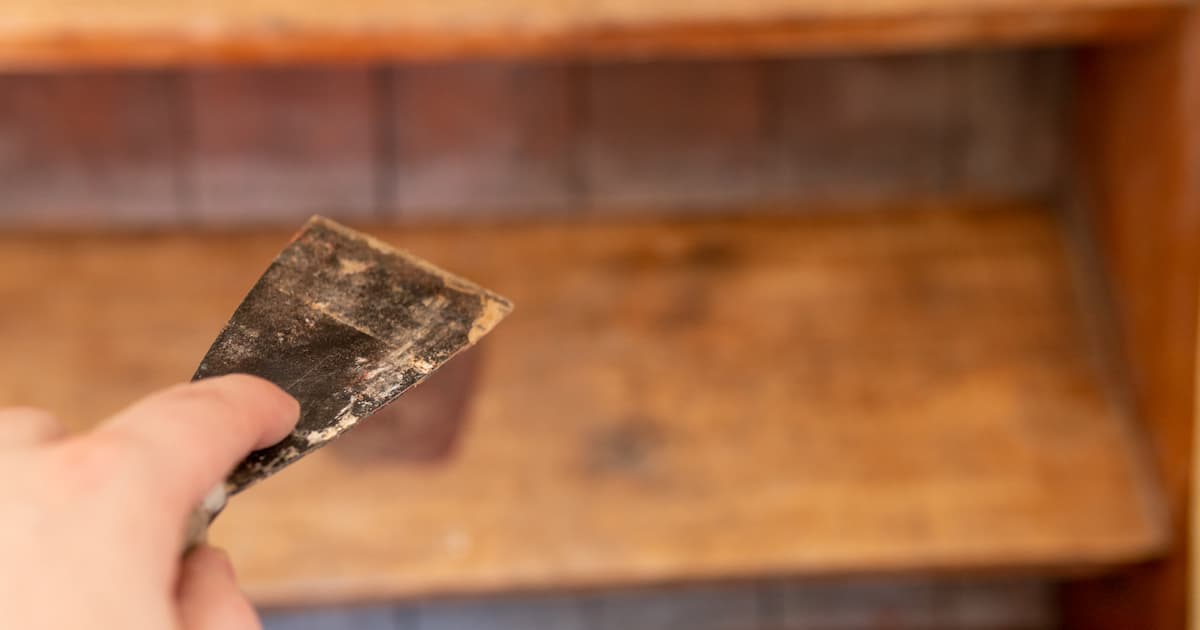 Une main qui tient un outil de décapage d'escalier sur fond d'escalier en bois