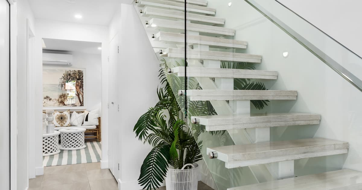Escalier à limon central avec balustrade en verre, plante et vue sur le salon.
