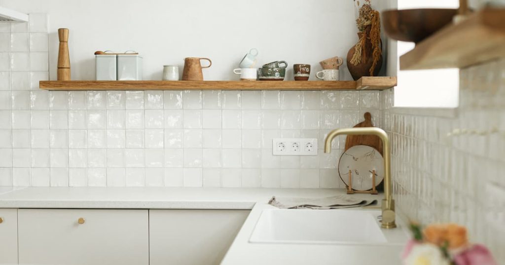 Conception moderne de cuisine minimale.  Élégantes armoires de cuisine blanche avec robinet en laiton, comptoir en granit et étagères en bois avec ustensiles dans une nouvelle maison 