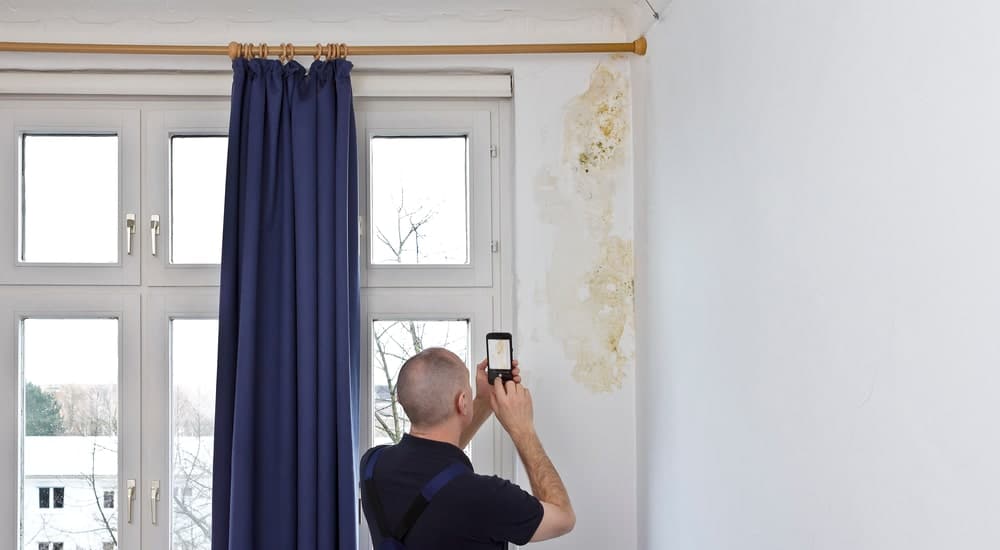 Homme qui prend en photo les dégâts provoqués par l'humidité sur son mur 


