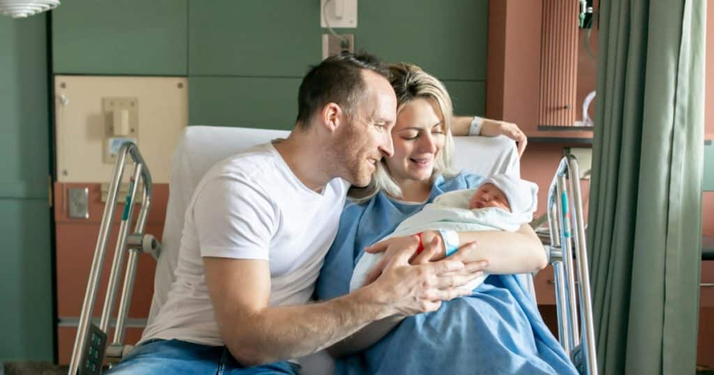 Deux parents se penchant sur leur nouveau-né assis sur un lit d'hopital