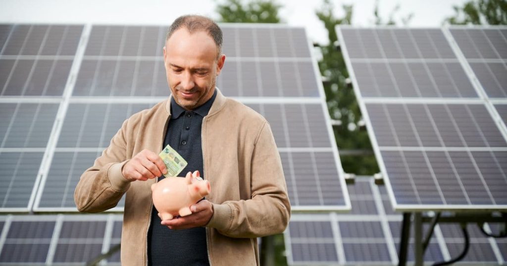 Homme devant des panneaux solaires mettant un billet dans une tirelire cochon