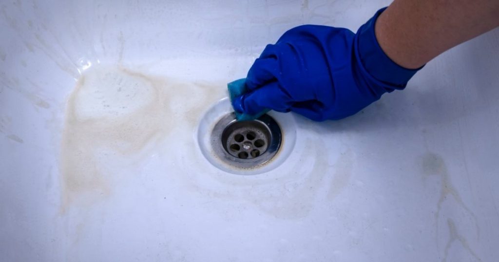 Une main équipée d'un gant en plastique nettoie le drain d'une baignoire sale