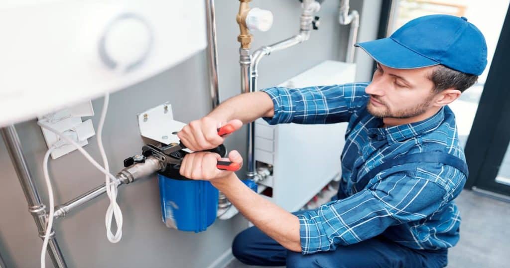 Jeune homme en vêtements de travail utilisant des pinces tout en installant un système de d'adoucisseur d'eau
