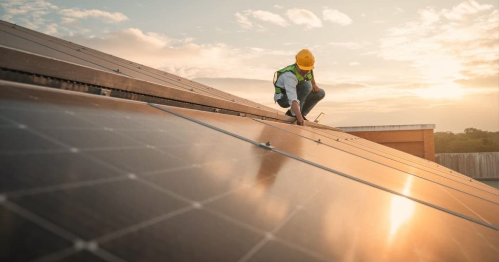 Installateur de panneaux solaires sur un toit entrain de vérifier l'installation avec le soleil qui tape.