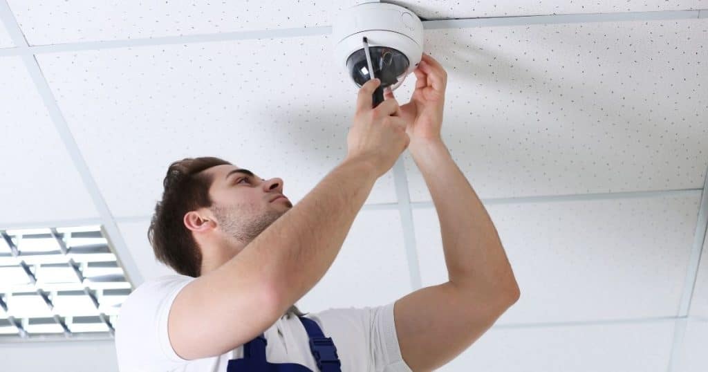 Personne avec un tablier bleu en train d'installer une caméra au plafond.