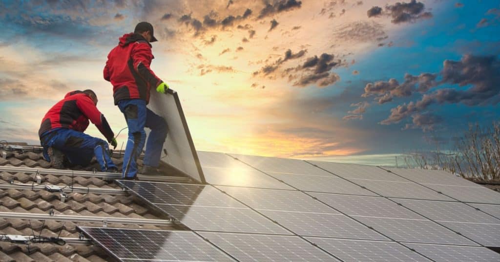 deux ouvriers installent des panneaux solaires sur le toit d'une maison 