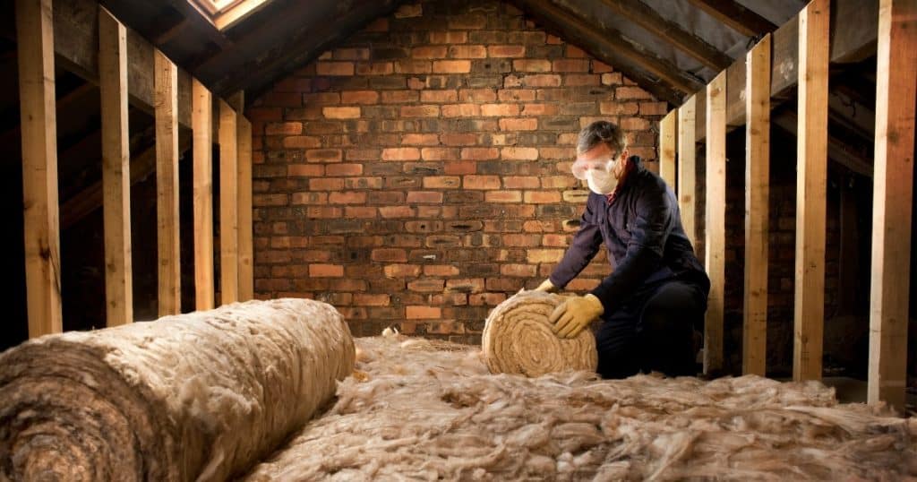 Une personne isole les combles d'un bâtiment