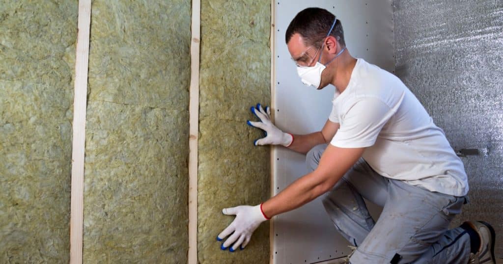 Isolation des murs à la laine de roche par un professionnel muni d'équipement de sécurité