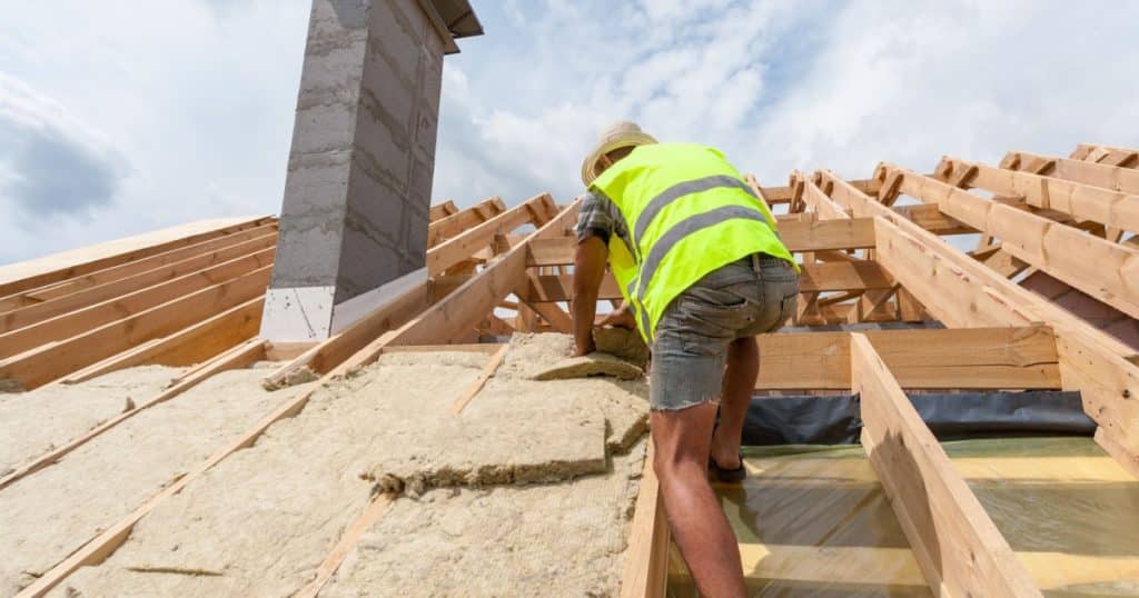 Un ouvrier place de la laine de roche entre les chevrons d'une toiture