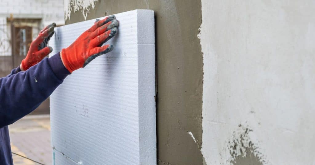 Isolation d'un mur par un professionnel avec une plaque de polystyrène.