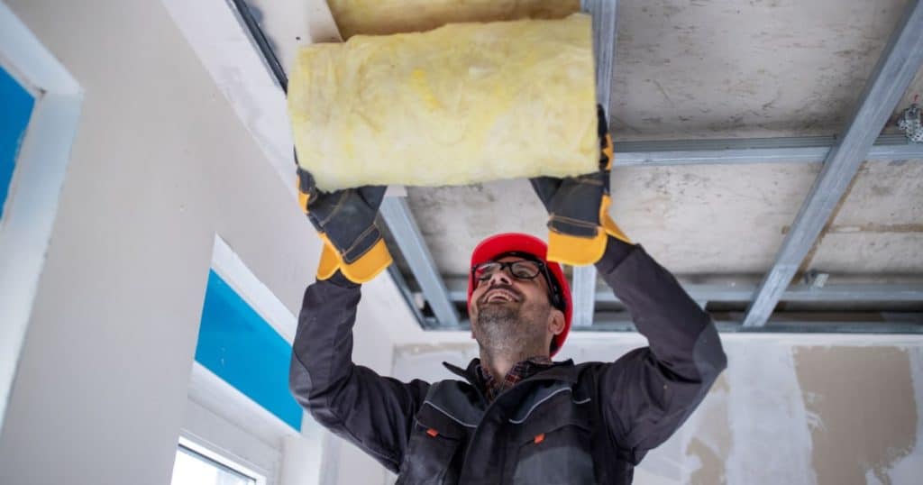 Isolation de plafond à la laine de verre par un professionnel doté de matériel de sécurité.