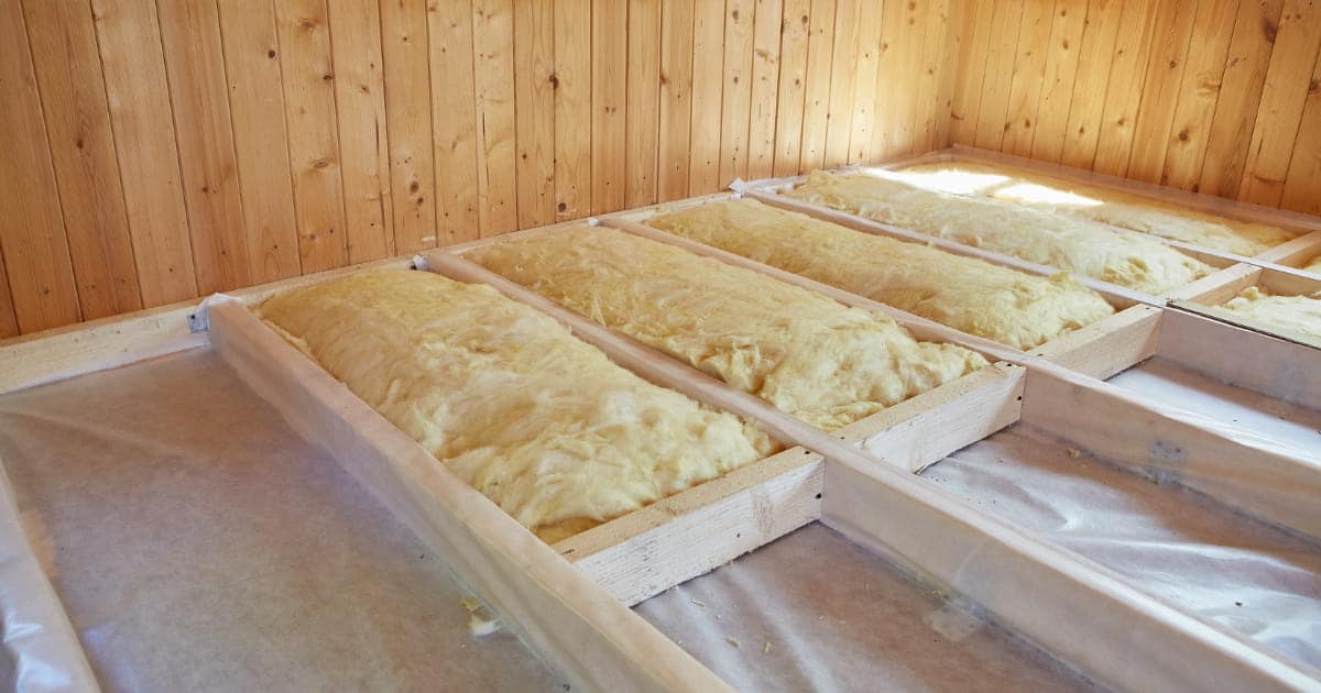 Isolation du sol avec de la laine minérale posée entre des solives en bois, sur un pare-vapeur.