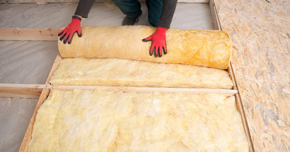 Un travailleur pose un isolant en rouleau sur le sol