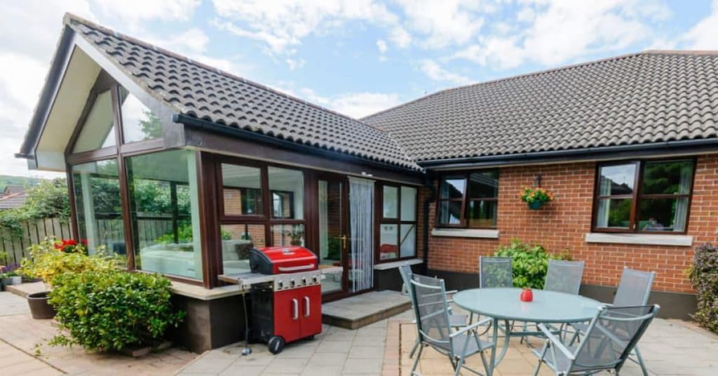 maison en briques avec véranda avec mur plein, table et chaises de jardin et barbecue à l'extérieur