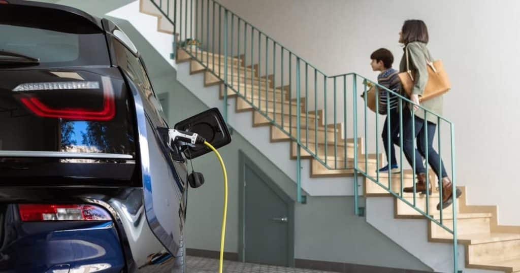 Un enfant et sa mère monte les escaliers du garage à côté d'une voiture en train d'être rechargée