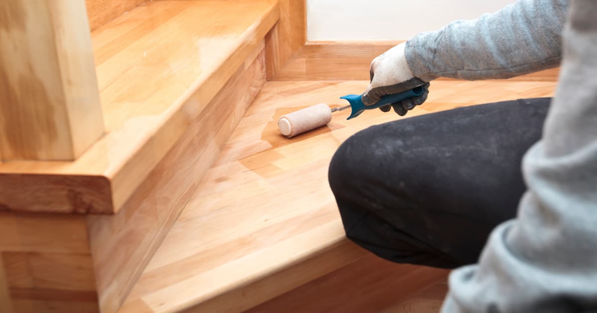 Le peintre  peint une marche d'escalier en bois vernie à l'aide d'un rouleau.