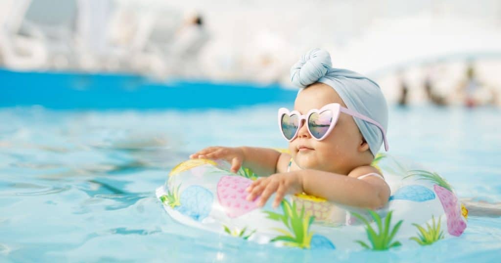 Bébé dans une piscine avec une bouée à motifs et des lunettes de soleil en forme de cœur. 