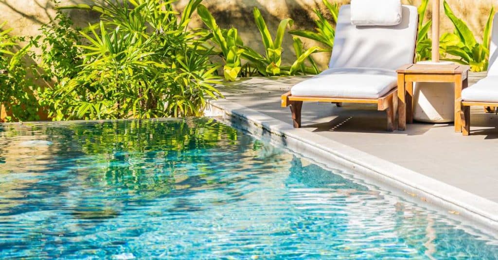 Piscine creusée à côté de plantes vertes et d'un transat en bois.

