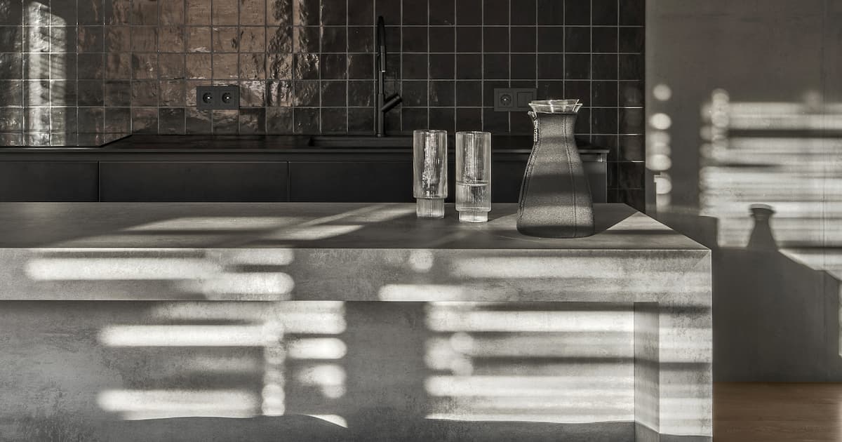 Petite cuisine intérieure aux couleurs grises et noires, mur en béton, portes coulissantes en verre. 
