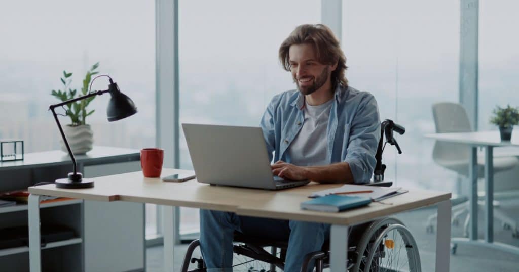 Un homme en chaise roulante travaille sur un ordinateur dans un bureau ouvert. 