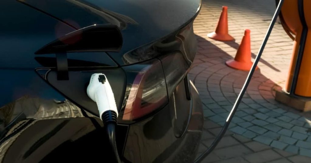 Voiture noire reliée à une prise de chargement électrique blanc