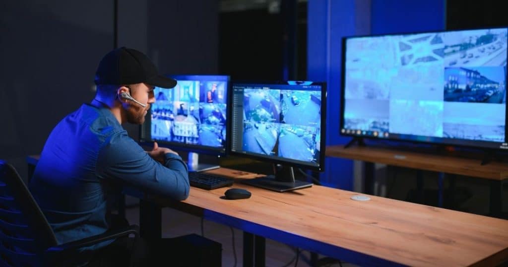 Agent de sécurité avec une oreillette et un microphone observant des vidéos de caméras de surveillance.