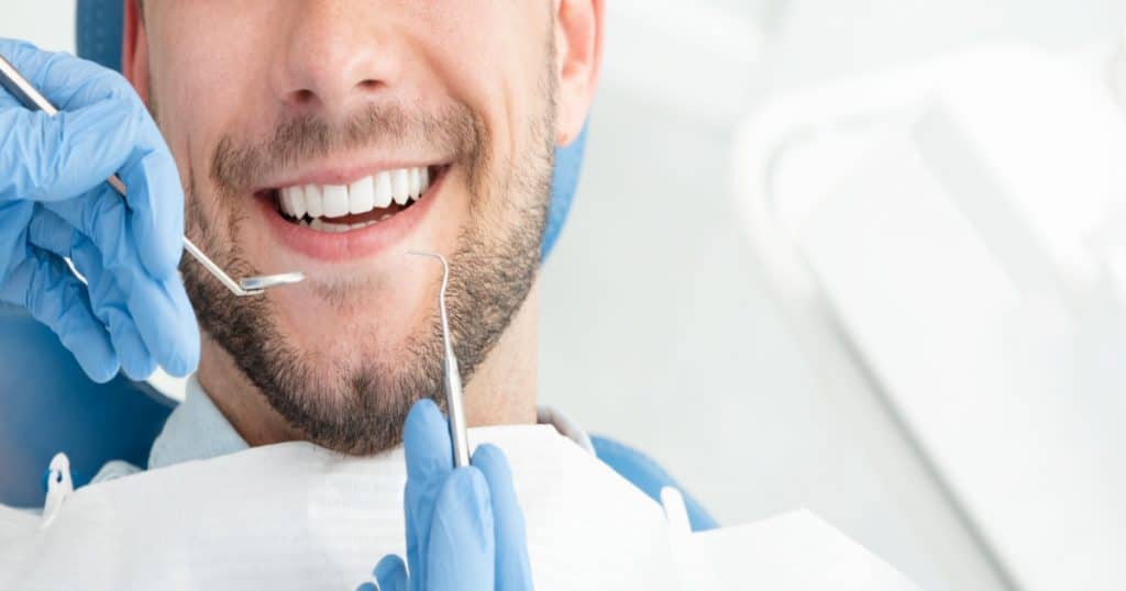 Un jeune homme souriant s'apprête à se faire examiner par un dentiste.