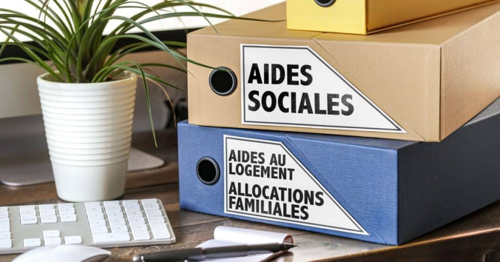 Table avec un clavier d'ordinateur, une plante et deux grosses fardes de dossiers, intitulées : Aides sociales et Allocations familiales.