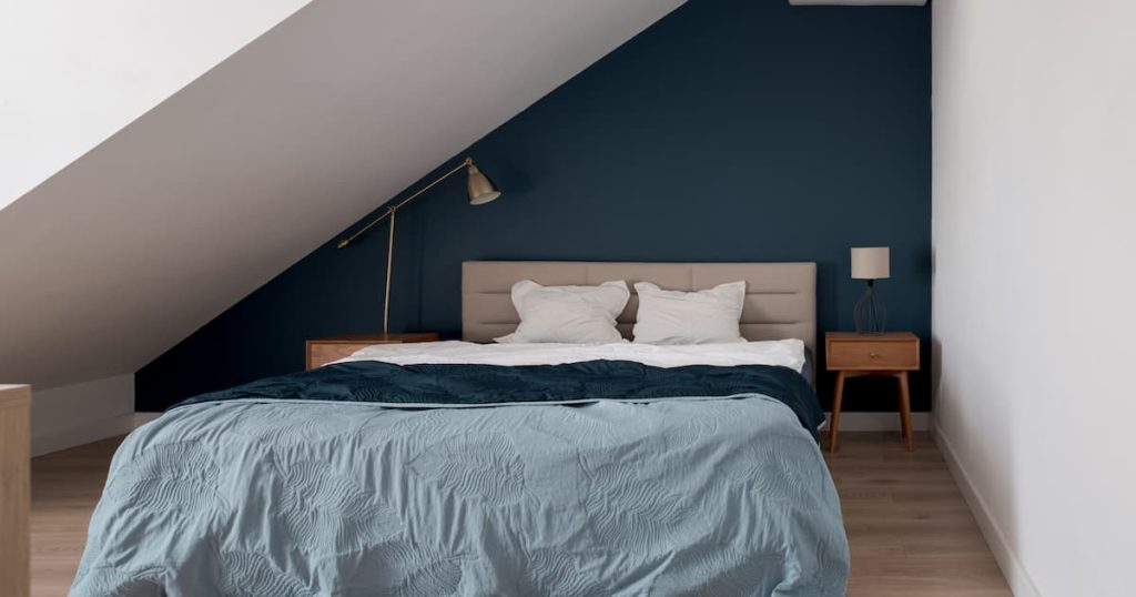 Chambre mansardée simple et confortable avec grand lit, mur bleu et table de chevet en bois